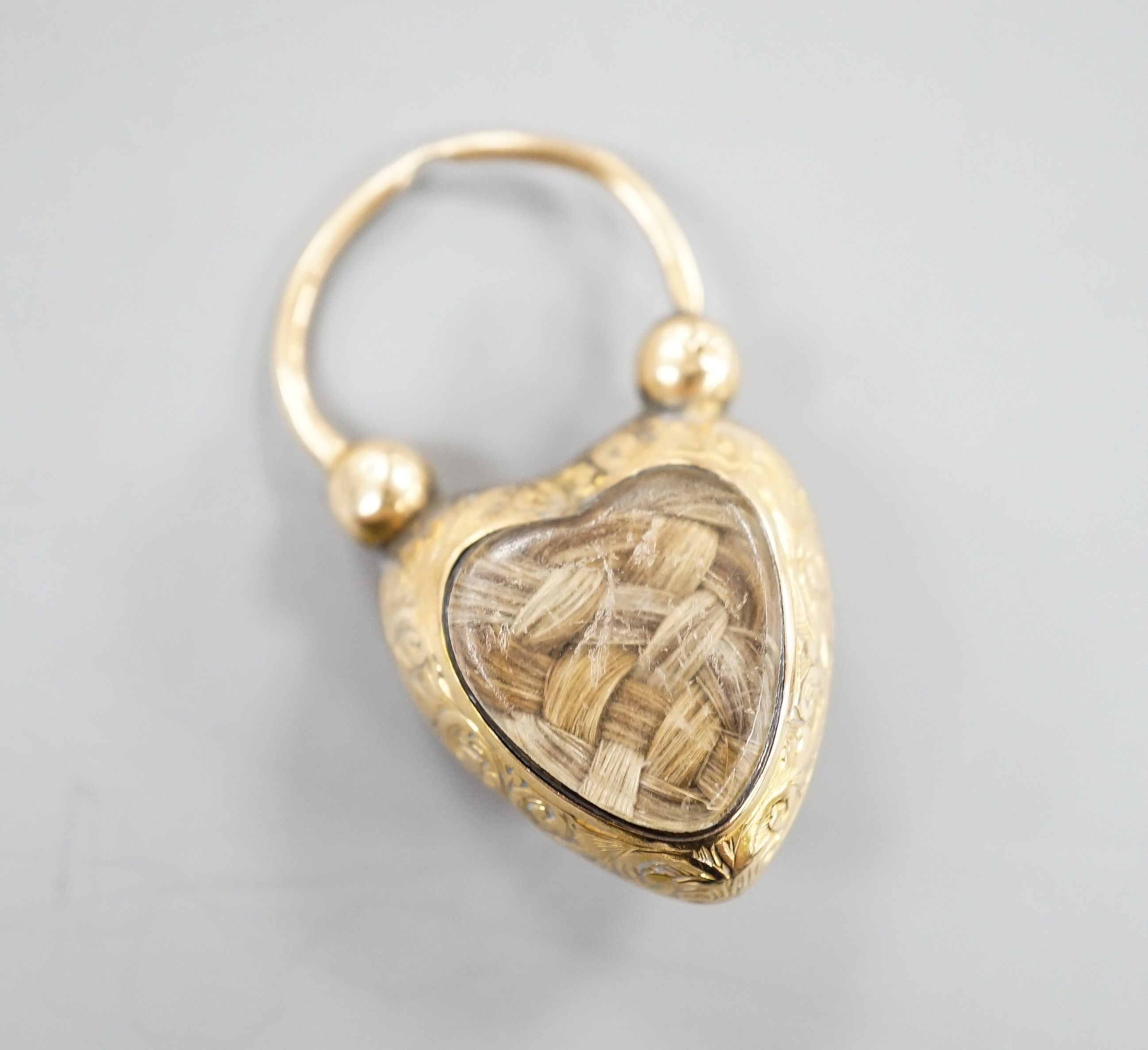 A 19th century engraved yellow metal and foil backed topaz set heart shaped mourning pendant, the back with plaited hair beneath a glazed panel, 31mm.